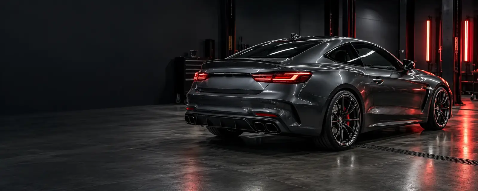 graphite coupe with polished bodywork and red inspection lighting in a dark workshop
