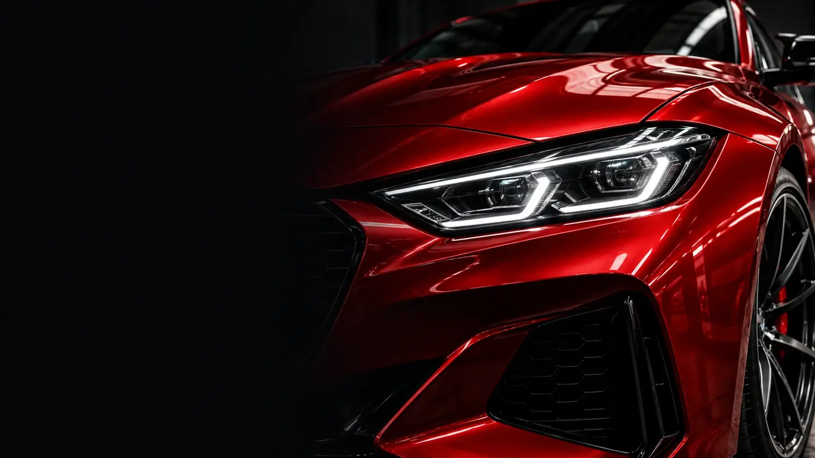 close-up of a glossy red performance car headlight in a dark workshop